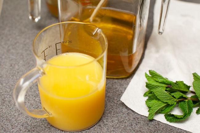orange juice in a measuring cup, tea in a jug and mint leaves on a counter