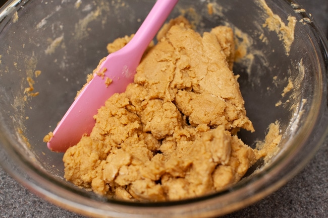 Peanut Butter Blossom Cookie dough a glass bowl with a pink rubber spatula. 