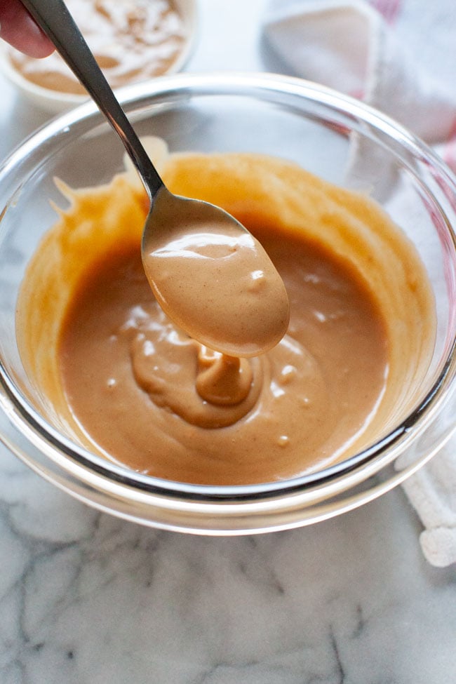 Peanut Sauce from thelittlekitchen.net peanut sauce on a spoon over a glass bowl with a napkin in the background