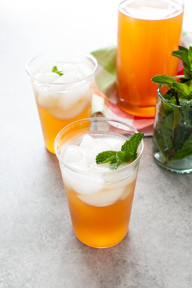 glasses with sweet tea vodka and lemonade with fresh mint in a glass on the side and a pitcher of the same drink in the background
